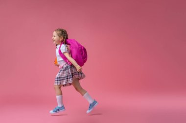 Okula dönün! Pembe arka planda koşan üniformalı çok çalışkan bir çocuk. Sırt çantalı çocuk. Küçük kız okul için hazır. Kavramsal okula kadar uzanan dinamik görüntüler. tatili başlat.