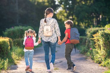 Annem öğrencilere yolda eşlik ediyor. Evrak çantalı çocuklar annelerini kucaklayarak okuldan çıkıyorlar. Ebeveyn ve ilkokul öğrencileri el ele tutuşuyor. başlangıç dersleri. Sonbahar.