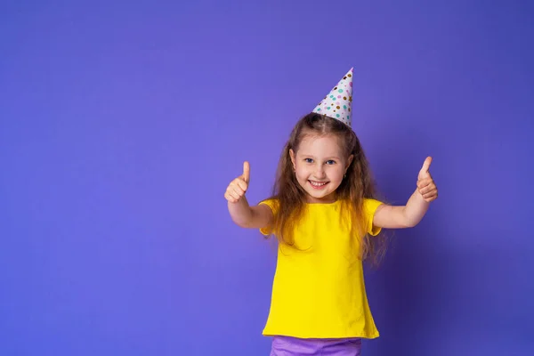 戴着节日礼帽 面带笑容的可爱而快乐的小女孩是快乐的 在紫色的背景上表现出认可的迹象 孩子的生日复制空间 — 图库照片