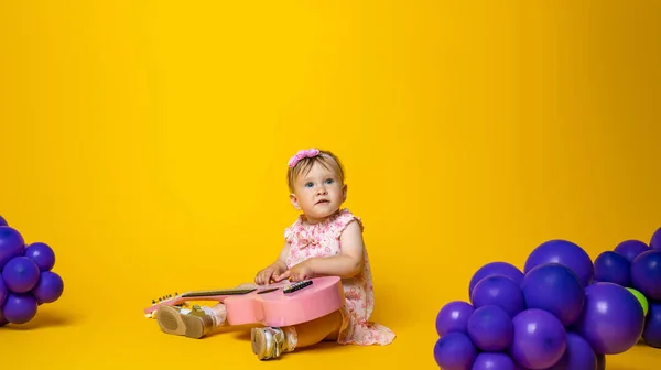 可爱的小宝宝在黄色的背景上弹奏吉它 气球是葡萄形状的 可爱的小孩在黄色背景下弹奏吉他 复制空间 儿童发展 — 图库照片