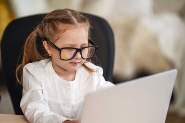 Küçük kız bilgisayarını evden öğrenmek için kullanıyor. Çocuk mutlu bir şekilde gülümser ve uzaktan bilgi alır. Dijital konsept e-öğrenme, salgın sırasında, karantina ve kendini izole etme. Uzak e- öğrenme.