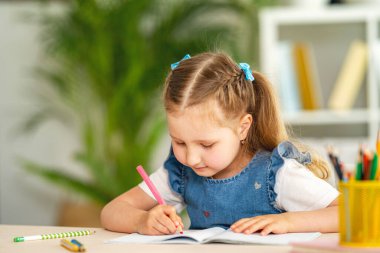 Küçük kız masada oturuyor, evde ödev yapıyor. Çocuk mutlu bir şekilde gülümsüyor ve karantina döneminde bilgi topluyor. Dijital konsept e-öğrenme, salgın sırasında, kendini izole etme. Okula geri dön..