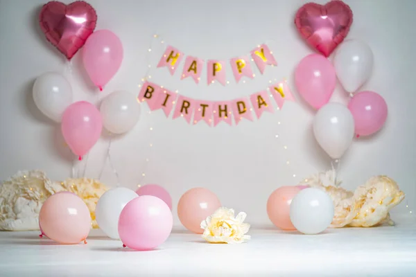 Happy Birthday! Children\'s decoration with glowing lights, birthday garland, pink and white balloons on a white background. Celebration of the first year of the baby. Decorated photo zone