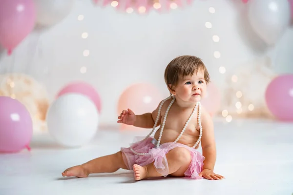 First year\'s birthday.a happy little girl in a pink tutu skirt crawls on a background with garlands and pink balloons, celebrating her first birthday. Birthday decoration.