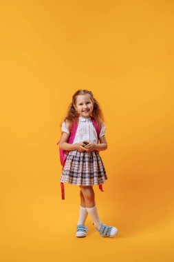 Sırt çantalı, elinde oyuncakla mutlu bir şekilde gülümseyen küçük kız stüdyoda pembe bir arka planda poz veriyor. Bu çocuk ilk kez okula gidiyor. Okula dönelim. Boşluğu kopyala