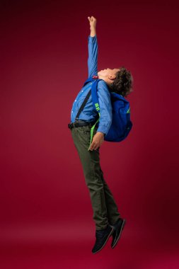 Kırmızı arka planda sırt çantalı, çalışkan, maksatlı bir okul çocuğu. Konsept okuluna kadar uzanan dinamik görüntüler. Tatilin başlangıcı. Okula dönelim. Çocuk çalışmaya hazır..