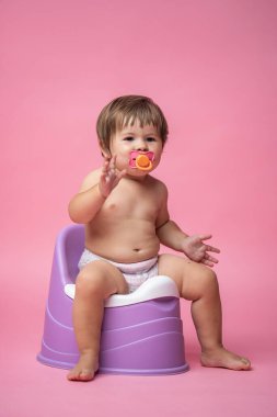 Altında emzik olan tatlı bir bebek tencerede oturuyor. Tuvalet ve tuvalet eğitimi. Küçük bir çocuk yararlı bir beceriye alışır. Hijyen. Bebek lazımlık lazımlığında oturuyor.