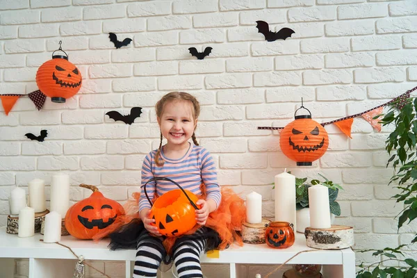 ハロウィン ハロウィンの魔女の衣装を着た女の子がお菓子やカボチャとテーブルに座っています トリックや治療 女の子は装飾された部屋でハロウィンを祝う — ストック写真