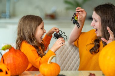 Mutlu bir aile. Neşeli anne ve kızı balkabaklarıyla masaya otururlar, gülerler ve örümceği gösterirler, evde Cadılar Bayramı kutlamalarında birbirlerini korkuturlar..