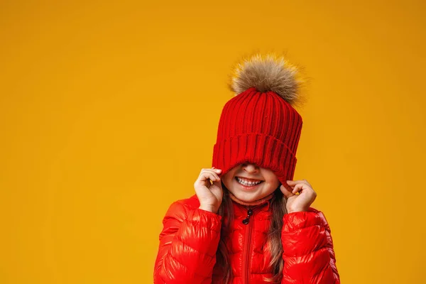 幸せな明るい女の子は赤いニット帽を目に引っ張ります 子供は明るい秋の服を着ており 秋の初めに満足しています スペースのコピー — ストック写真