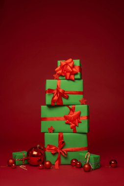 Mutlu Noeller! Yeni yıl kutlaması için hazırlanıyorum. Kırmızı kurdeleli ve Noel toplu yeşil hediye kutularından oluşan Noel kompozisyon grubu stüdyoda kırmızı arka planda duruyor. Yerleşim planı. Boşluğu kopyala.