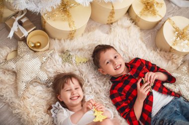 Mutlu Noeller! Neşeli küçük oğlan ve kız hediyelerle süslenmiş Noel ağacının yanındaki halıya uzanıyorlar. Çocuklar sabahları eğleniyor. Yukarıdan bak. Erkek ve kız kardeş Noel 'de çok sevindi..