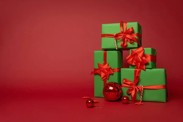 Merry Christmas! Preparing for New year celebration. Christmas composition group of green gift boxes with red ribbons and Christmas balls stand on a red background in the Studio. Layout. Copy space.