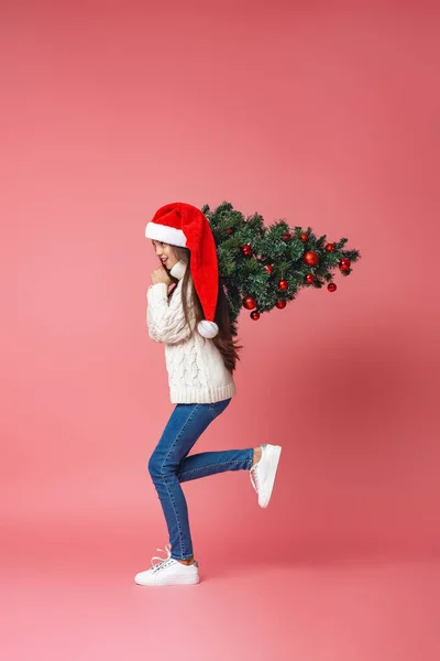 身穿针织毛衣 头戴全长圣诞老人帽 肩上挂着红色圣诞彩球的快乐少女 走在绿色的背景上 为圣诞节做准备 — 图库照片