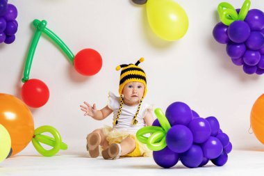 Çekici, çizgili şapkalı, balonlu, meyve arka planında poz veren güzel bir kız. Bebek arka planda meyve şeklinde balonlarla stüdyoda oturuyor. Yaz konsepti, vitaminler, meyve. Boşluğu kopyala