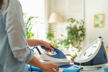 Yakın çekim, yan görüş, bir kadın ütüyü güneşli bir günde yıkadıktan sonra ütü masasının terazisinden temizler. Modern buhar sistemi, yeni cihazlar.