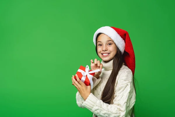 圣诞快乐 快乐的小女孩戴着圣诞礼帽手里拿着礼品盒 背景是绿色的 孩子打开礼物时感到很惊讶 一个意想不到的惊喜 平安夜 — 图库照片