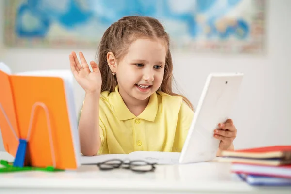 学校に戻る 幸せな学校の女の子は タブレットコンピュータで机の上に座って女の子の宿題やオンライン教育を行う 子供がビデオ会議で挨拶を言う — ストック写真
