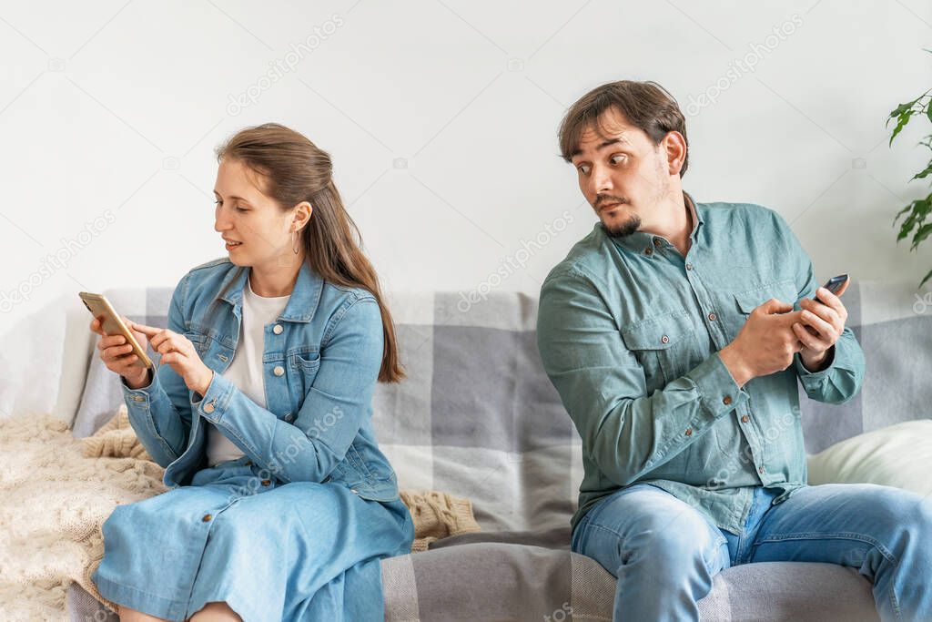 jealous husband spies on his wife, suspicious man tries to read messages on his girlfriend's mobile phone curiously peeking peering while she is not looking he is looking. Distrust in relationships