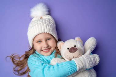 Dört yaşında, sarı saçlı, örgü kazaklı mutlu bir kız çocuğu. Gülümsüyor ve stüdyoda leylak bir arka planda oyuncak ayıya sarılıyor. Oyuncak onun arkadaşı. Kış zamanı. Hafta sonu tatili