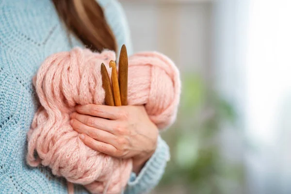 Close-up of a woman holding a thick pink yarn, wooden needles and a hook. Concept of freelance creative work and life. Women\'s hobby.