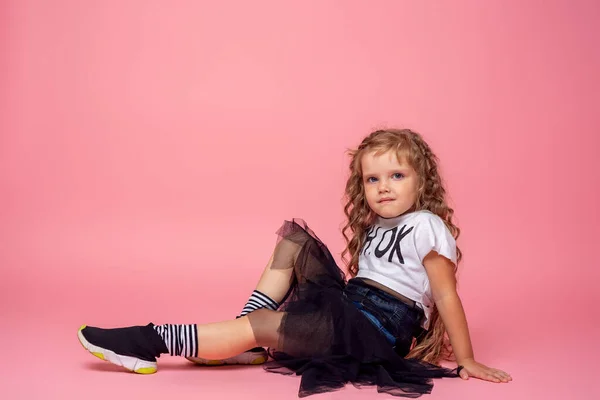 时髦的小女孩 卷曲的头发 穿着时髦的衣服 坐在粉色的背景上 儿童的情感形象 — 图库照片