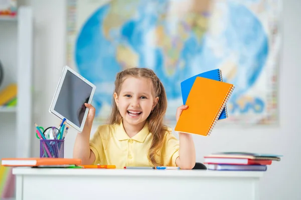 学校に戻る 机の上に座っている幸せな女子高生 その少女はタブレットを使って宿題をする 感染症の流行期のオンライン教育は — ストック写真