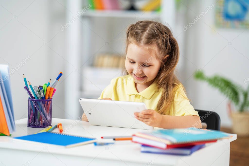 Back to school. Happy little schoolgirl sitting at her Desk. The girl does her homework using a tablet computer. online education in the period of the epidemic covid 19