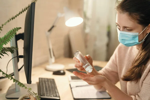 Business working in a mask works at a computer. Treating hands with a sanitizer. Work at home. Washes hands with disinfectant gel. Protection from coronavirus.