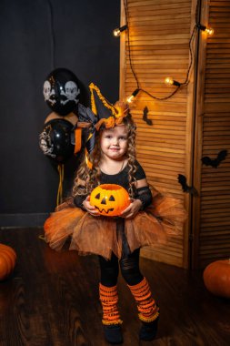 Mutlu Cadılar Bayramı! Balkabaklı şirin küçük cadı tatil süslemelerinin üzerinde duruyor. Çocuk Cadılar Bayramı için hazırlanıyor. Çocuk elinde balkabağı şeklindeki fenerle korkuyor.