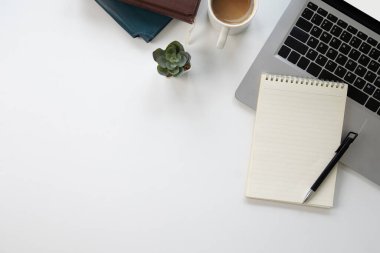 Beyaz dizüstü bilgisayarın üzerine serilmiş beyaz defter, üst görünüm