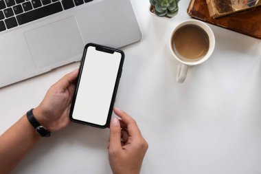 Genç bir kadının eli beyaz bir masada telefon kullanıyor.