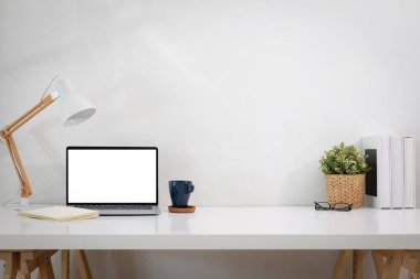 Laptop, lamba, defter, kahve fincanı, bardak, not defteri, saksı bitkisi olan çalışma masası. ön görünüm