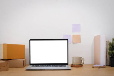 Üzerinde paket kutuları olan çalışma masası ve beyaz ekranlı laptop.