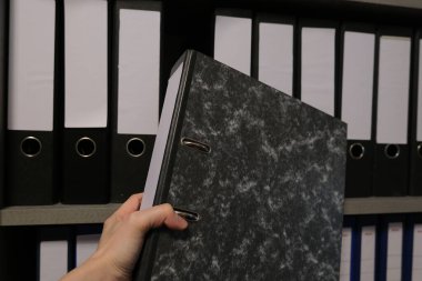 Raftan siyah bir mermer ofis klasörü çıkarmak, iş yerindeki düzen kavramı, dosyalama ve belge yönetimi