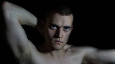 Siyah bir arka planda eli başının arkasında olan bir adamın portresi.