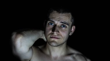 Siyah bir arka planda eli başının arkasında olan bir adamın portresi.