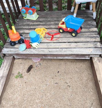Childrens sandbox filled with light sand with a wooden edge. Bright plastic toys for children are laid out on a wooden platform next to the sandbox. Childrens games in the open air