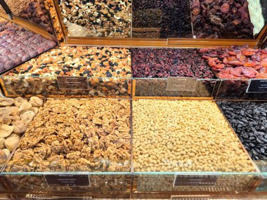 Vitrindeki cam kaplarda düzgünce sergilenmiş kurutulmuş meyve ve fındık çeşitleri. Çeşitli fındık çeşitleri - ceviz, çam fıstığı, kurutulmuş meyve - kuru üzüm, kızılcık, kuru kayısı, kuru erik