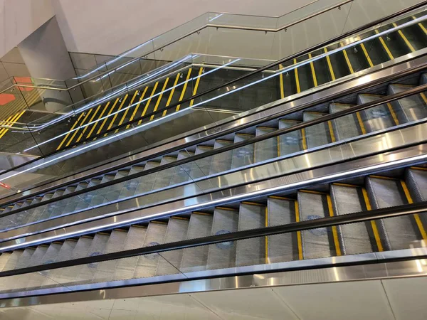 Yolcular modern bir havaalanı terminalinde uzun ve parlak bir koridorda yürürler. Büyük pencerelerden akan güneş ışığı yerde ve duvarlarda uzun gölgeler oluşturarak mimari çizgileri aydınlatıyor..