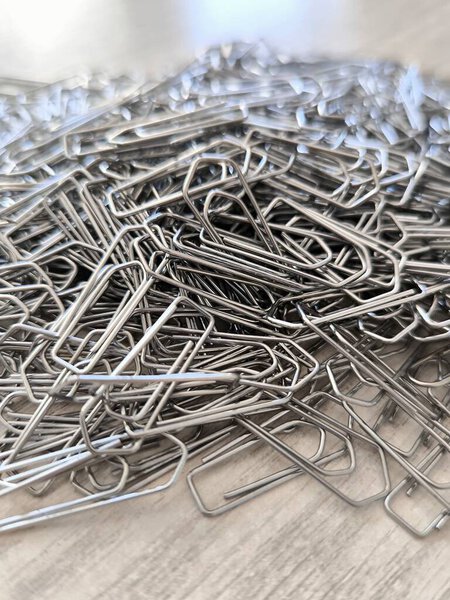 A macro shot of metal paper clips scattered across a light wood surface, the image taken from above shows the texture and shape of each clip