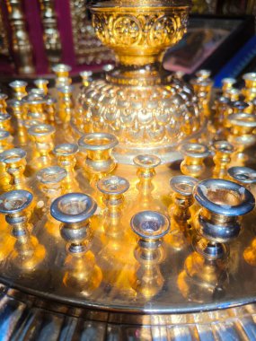 Altın renkli metalden yapılmış antik bir kilise şamdanının tepesine yakın çekim. Detaylar bir daire içinde dizilmiş küçük mum tutucuları vurgular.