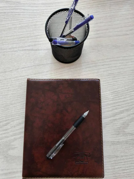 Şeffaf bir siyah tükenmez kalem kahverengi bir telefon rehberinin üzerinde yatar. Yakınlarda bir ağlı kalem tutacağı var..