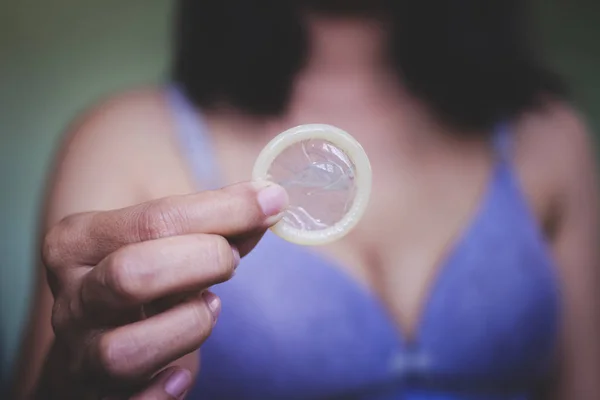 Woman showing a condom on bed, Focus on the condom in the foreground