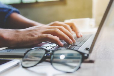 Evde dizüstü bilgisayar cıyla çalışarak blog yazıyor. Adam elleri üzerinde