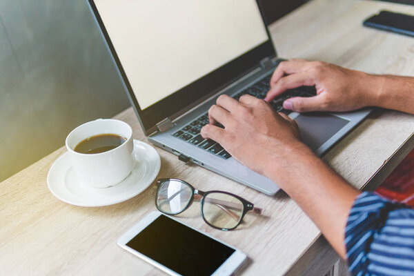 Man's hands typing on a laptop that is on a wooden desk with a m
