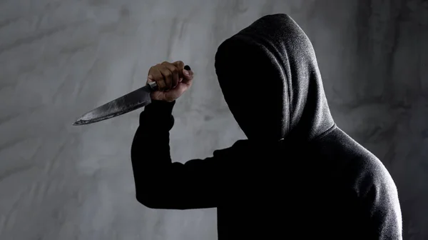 Dangerous hooded man standing in the dark and holding a knife Fa