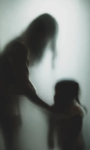Ghost concept shadow of mother who is strangling the neck of the child behind the matte glass blurry hand and body soft focus