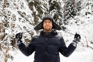 Kulağı olan kürk kış şapkalı adam gülümseyen portre flep. Ormanın içinde aşırı