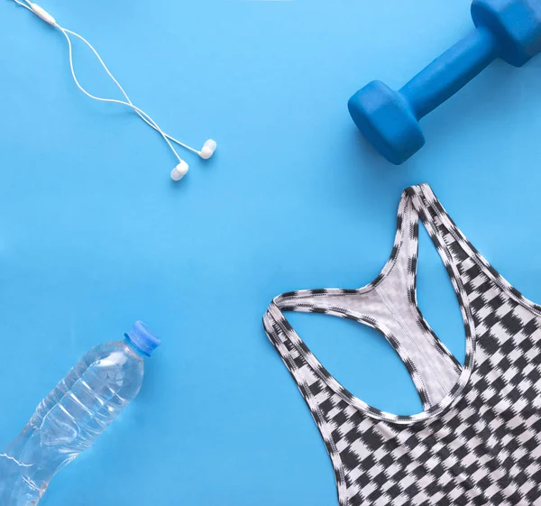black white sports top, blue dumbbell, headphones, water bottle on blue background,  flat lay